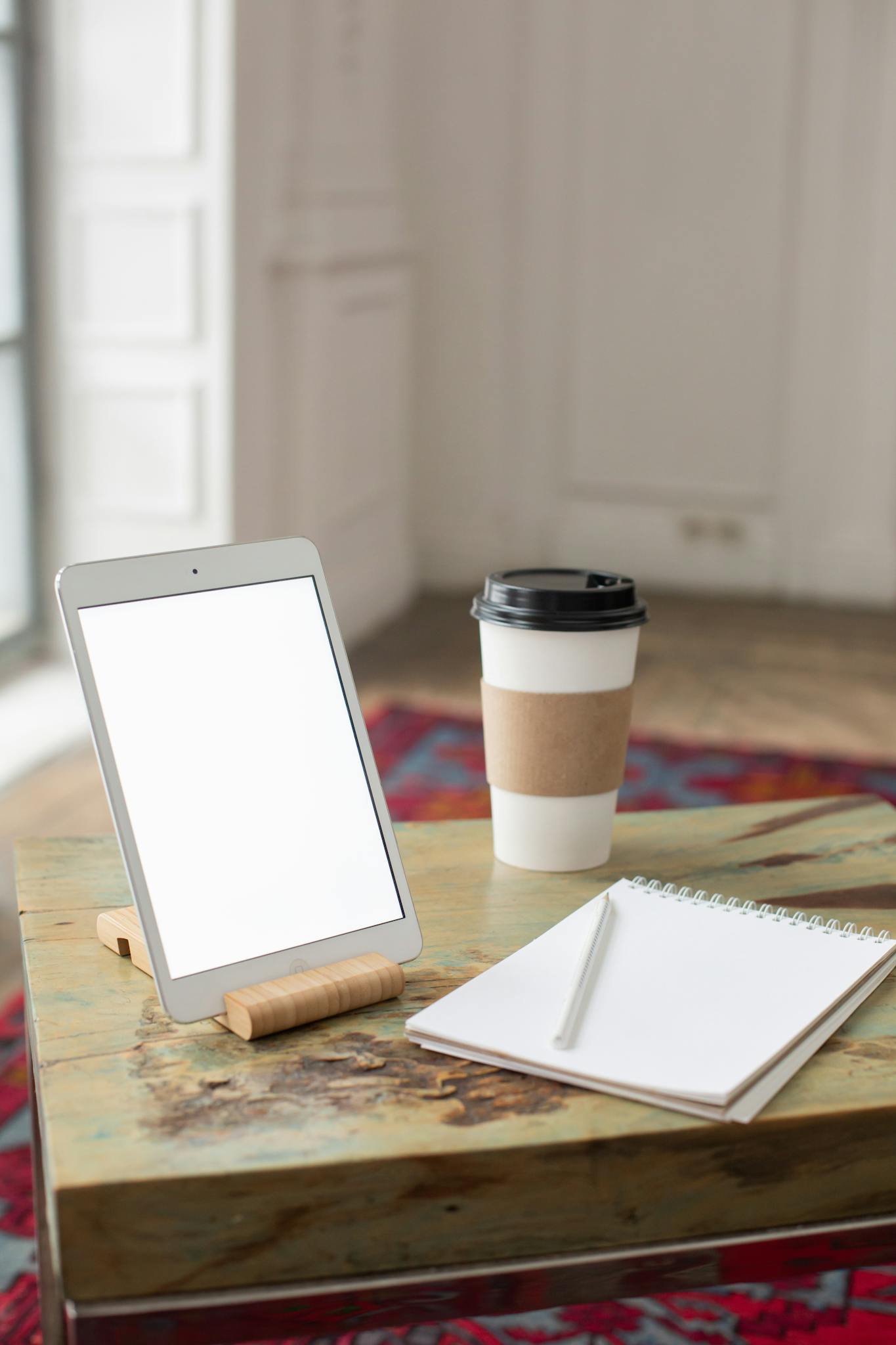 A clean and minimalist workspace featuring a tablet, coffee cup, and notebook on a wooden table.