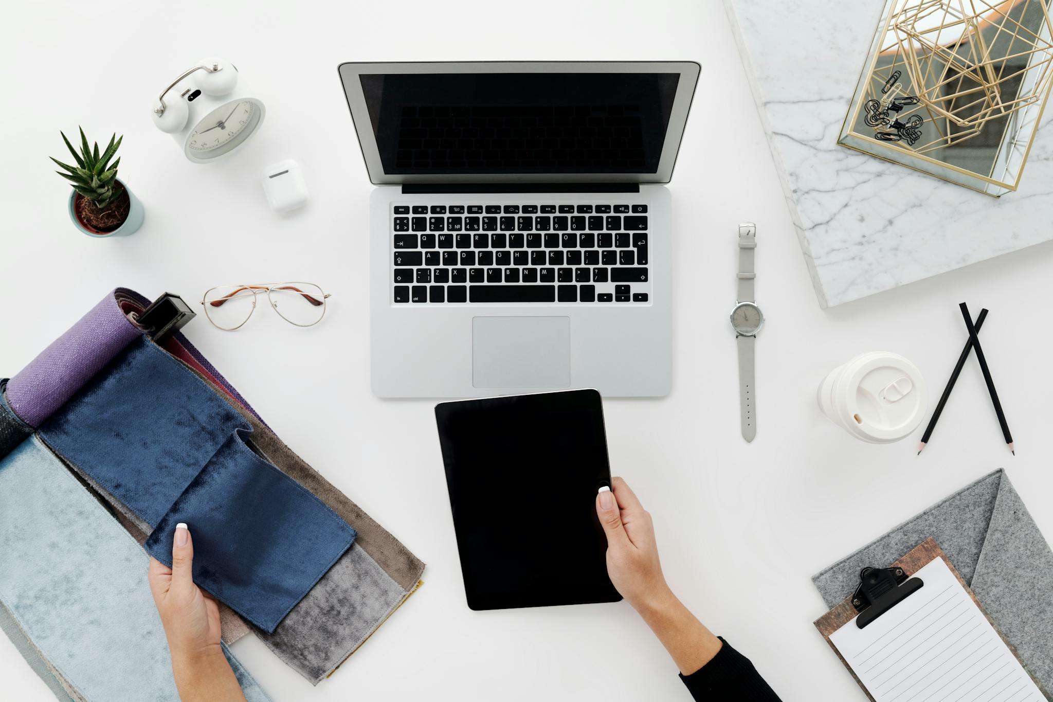 Creative workspace setup with laptop, tablet, and designer tools on a white table.